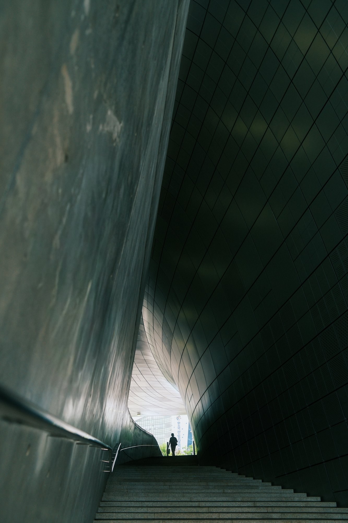 Lone figure at the top of stairs between curved walls